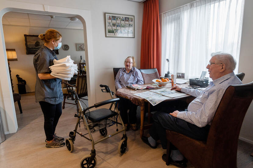 Zorgmedewerker met mondkap helpt twee oudere mensen