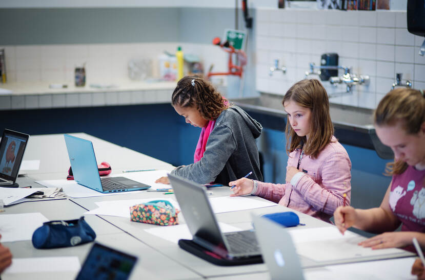 Drie leerlingen zijn in een klaslokaal aan het werk achter hun laptop