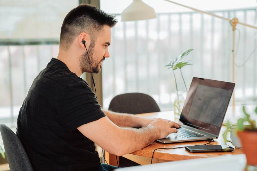 Man zit aan een bureau naar zijn laptop te kijken met zijn oordopjes in zijn oren