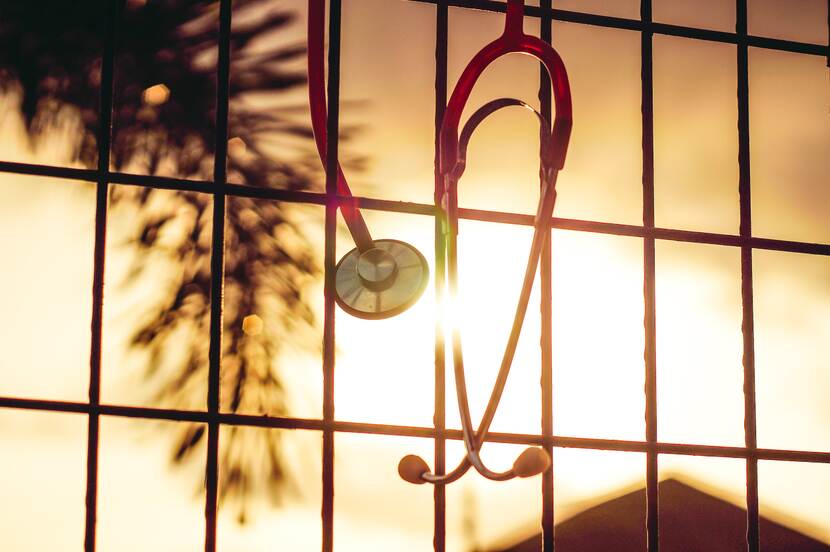 Stethoscoop hangt aan een hek met zon en palmboom op achtergrond